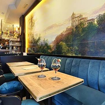 The dining room at Le Village Madeleine: blue velvet banquettes, wooden tables and a large mural